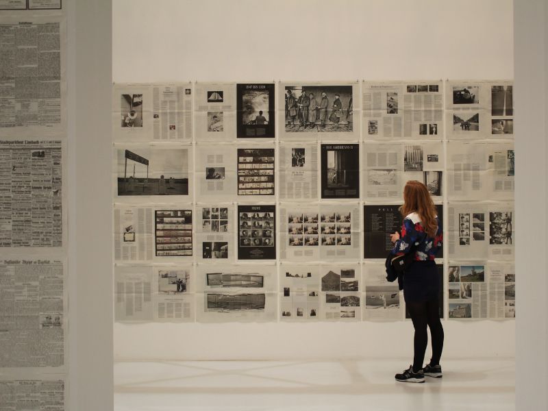 A woman looks at magazine pages on the wall of a gallery.