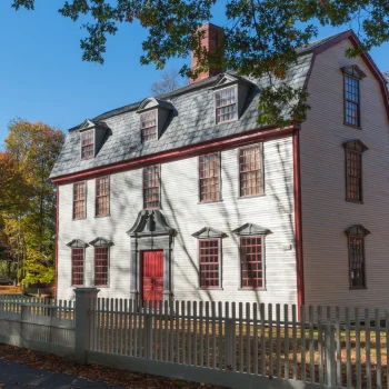 Historic building of three floors, with barn style roof and large red door.