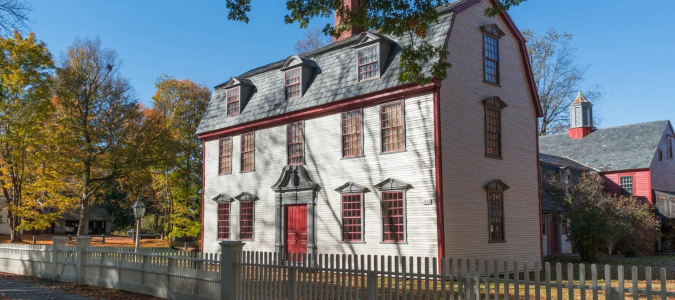Historic building of three floors, with barn style roof and large red door.